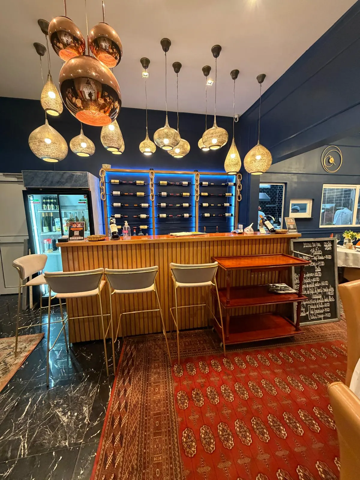 Bar en bois du restaurant, tabourets hauts et suspensions cuivrées sur murs bleu roi