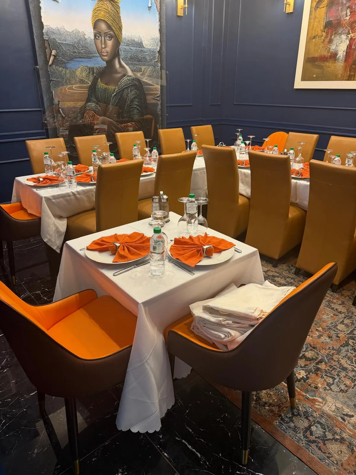 Tables carrées nappées de blanc et dressées de serviettes orange, fauteuils à assise orange au premier plan